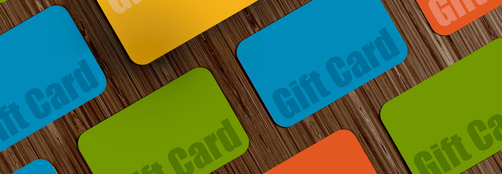 A variety of colorful gift cards are scattered across a wooden surface. The cards are in shades of green, blue, orange, and yellow, each with the text Gift Card written on its surface.