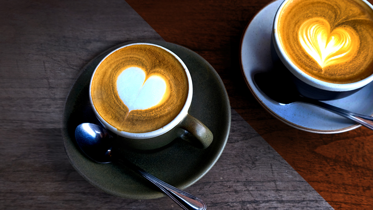 Two cups of cappuccino with heart-shaped latte art sit on saucers with spoons. The image is divided diagonally, with one cup in a dim setting and the other in bright lighting, showcasing different ambiance effects on the wooden table.