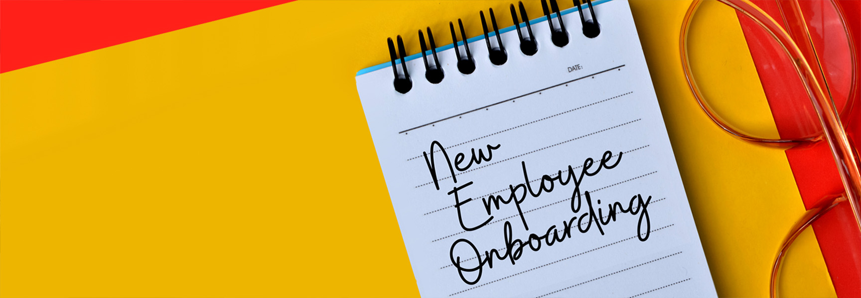 A notebook with New Employee Onboarding written on it is placed on a yellow and red background. There is a pair of glasses next to the notebook.