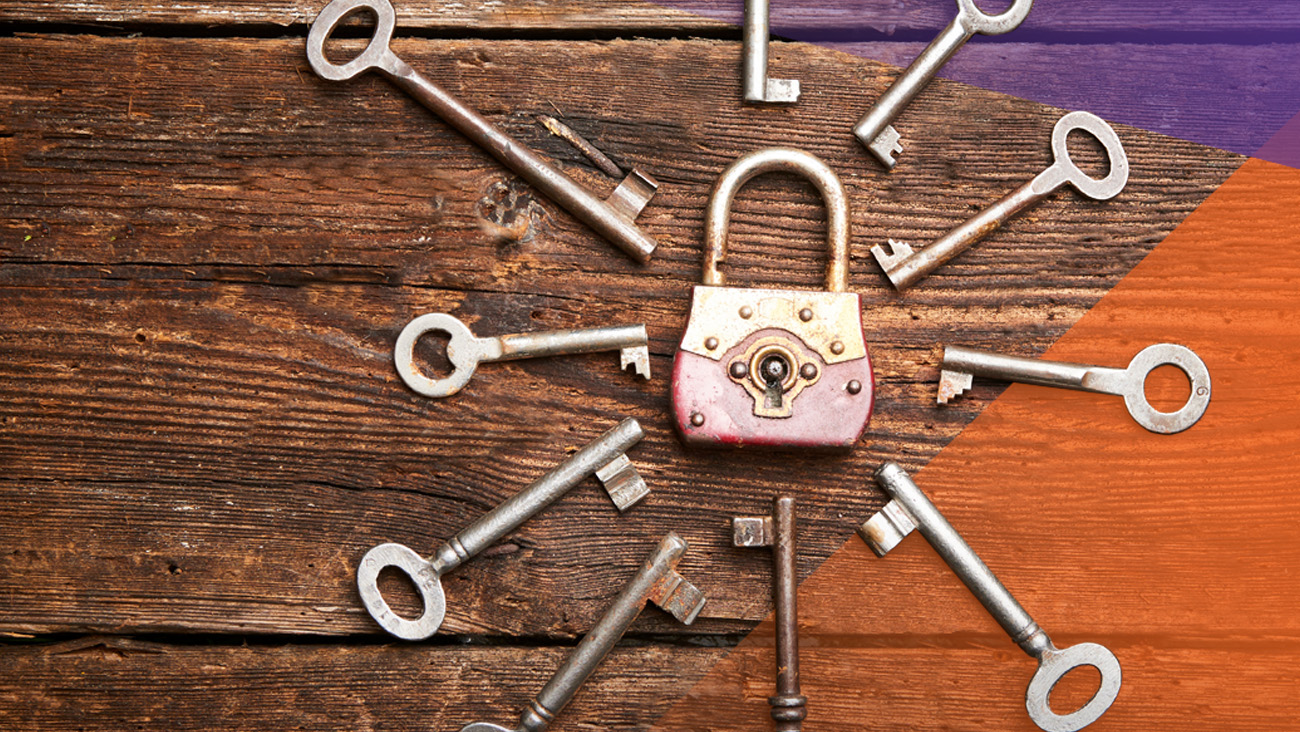 A vintage padlock surrounded by a circle of nine old-fashioned metal keys on a rustic wooden surface. The arrangement forms a radial pattern with the padlock in the center.