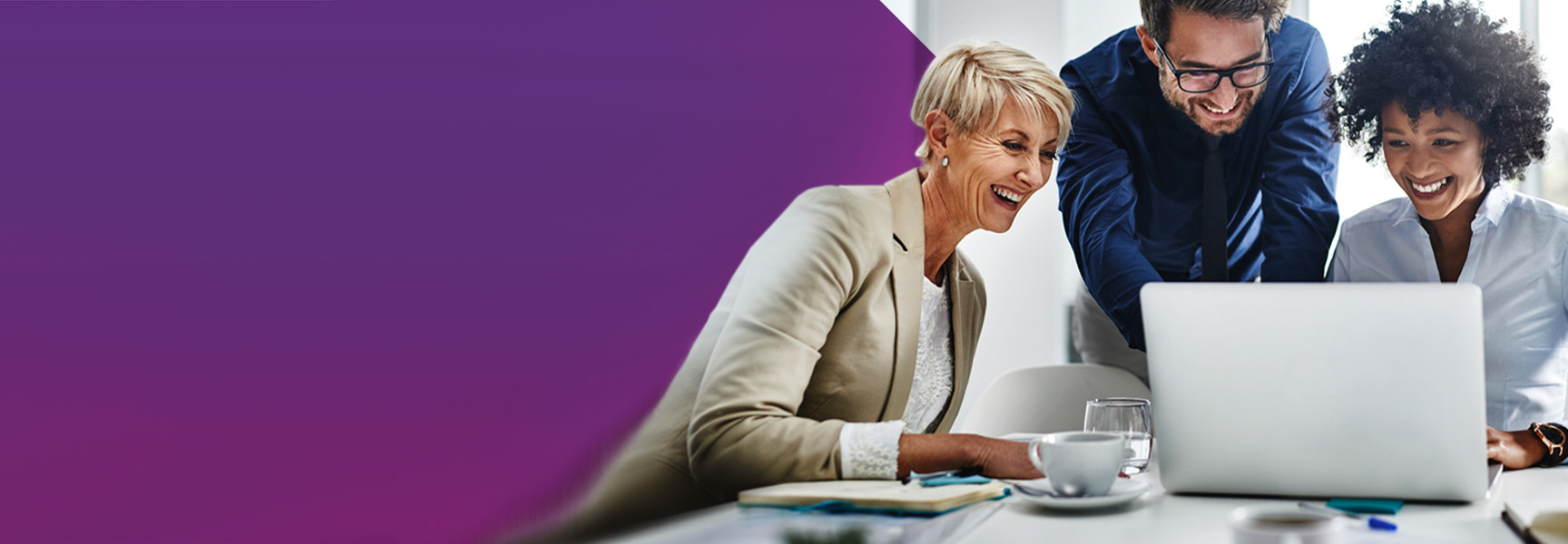 A group of three people smiling and looking at a laptop in an office setting. The person on the left is seated with a cup of coffee, while the other two stand, leaning in to view the screen. The background features a purple gradient.