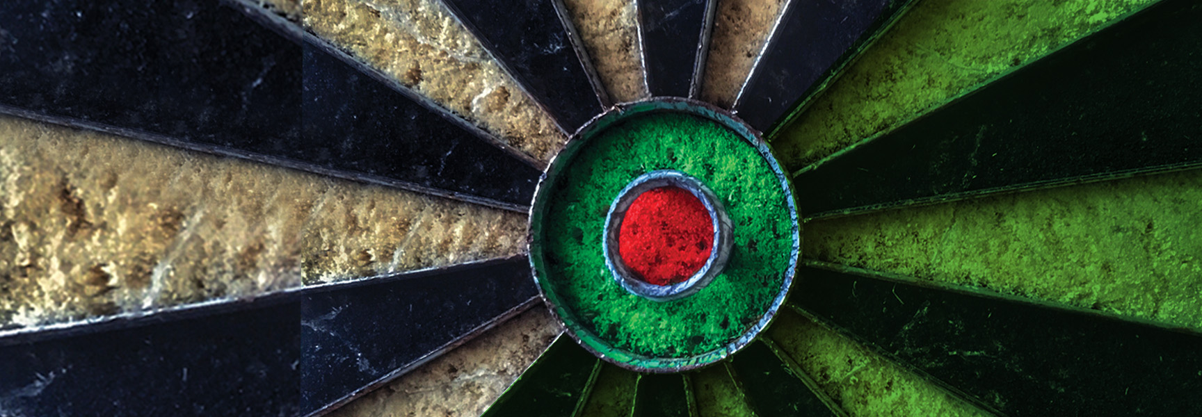 Close-up of the bullseye area of a dartboard. The central red circle is surrounded by green, with alternating black and green sections radiating outward. The surface has a textured, worn appearance.